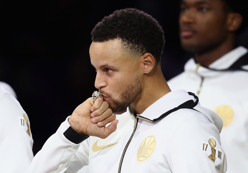 Stephen Curry #30 of the Golden State Warriors kisses his 2017-2018 Championship ring prior to their game against the Oklahoma City Thunder at ORACLE Arena on October 16, 2018 in Oakland, California. Ezra Shaw/Getty Images/AFP