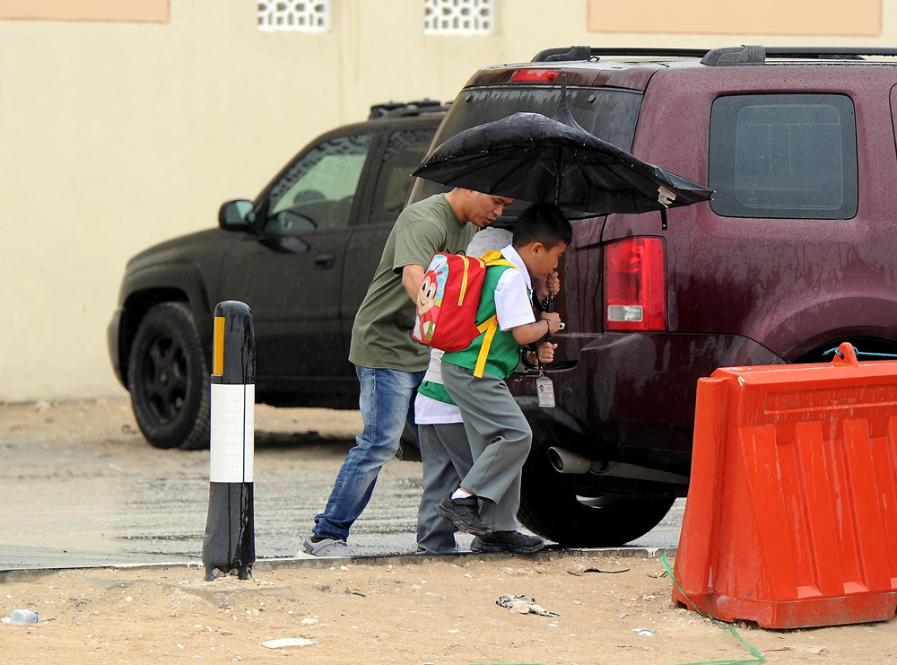 FILE PHOTO: School children take shelter under an umbrella in rain at Abu Hamour. Abdul Basit © The Peninsula