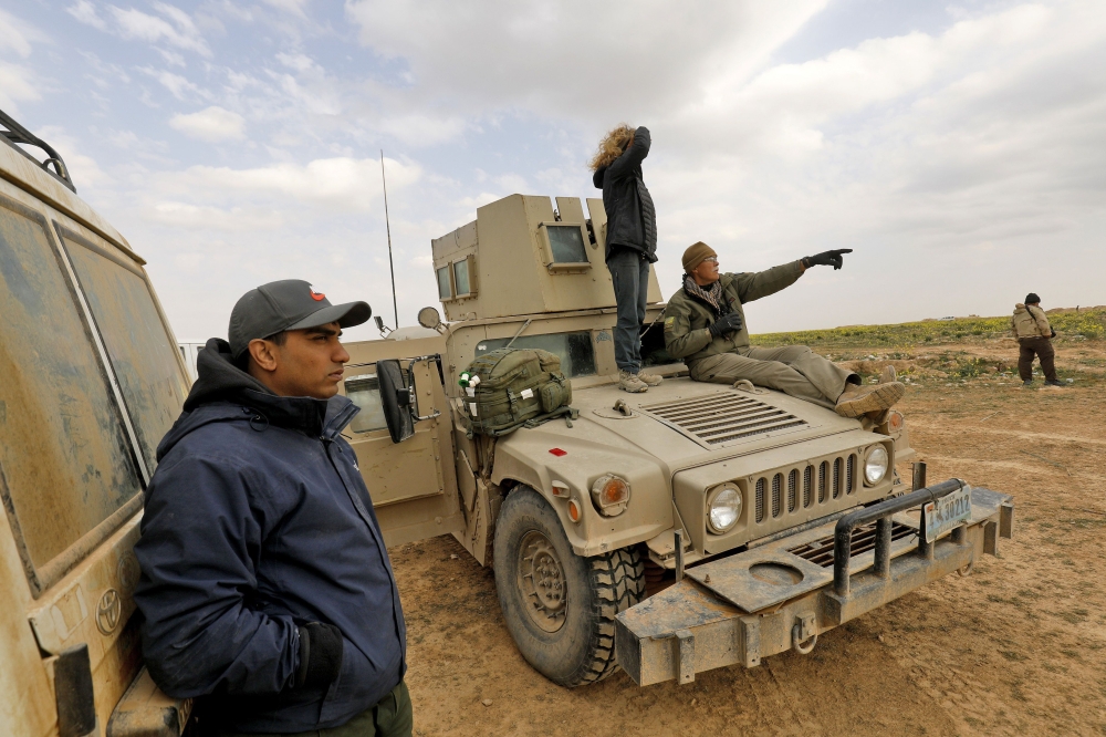 Paul Bradley (R), a volunteer with the Free Burma Rangers (FBR), sits on a US-made Humvee at a plateau overlooking the embattled Baghouz area in the eastern Syrian province of Deir Ezzor, on February 14, 2019. AFP / DELIL SOULEIMAN
