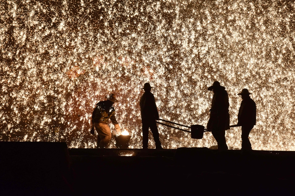 This photo taken on February 18, 2019 shows a Chinese blacksmith (L) throwing molten metal against a cold stone wall to create a shower of sparks, on the eve of the Lantern Festival, which marks the end of Lunar New Year celebrations, in Nuanquan, in Chin