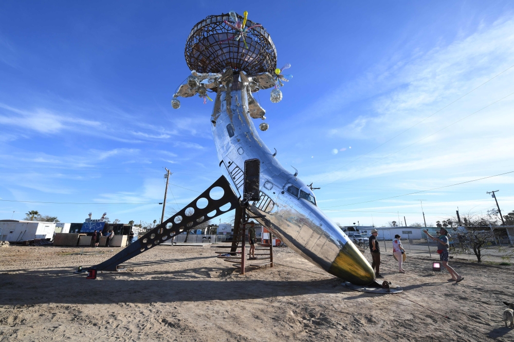 People visit an installation sculpture of a crashed plane by artist Randy Polumbo, on the first day of the Bombay Beach Biennale, March 22 2019 in Bombay Beach, California.  AFP / Robyn Beck