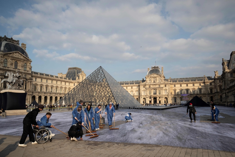 French contemporary artist and photographer Jean Rene (L), aka JR, is helped by volunteers during preparation works of his installation in the main courtyard Cour Napoleon of the Louvre Museum in Paris on March 27, 2019, as part of the 30th anniversary ce