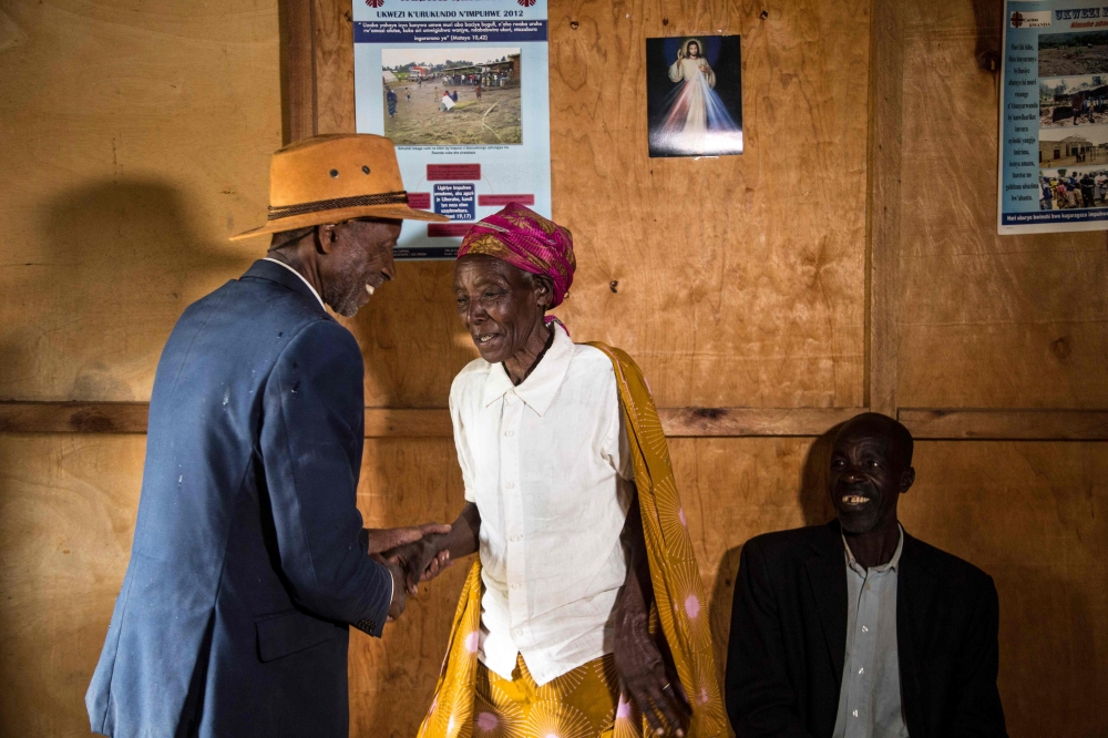 Jean-Bosco Gakwenzire (L), 65, of Tutsi ethnicity shakes the hand of Rose, 72, wife of his old school mate, Pascal Shyirahwamaboko (R), 68, both Hutu's, following Sunday mass at their church in the sector of Mutete, in Byumba city.  AFP / Jacques Nkinzing