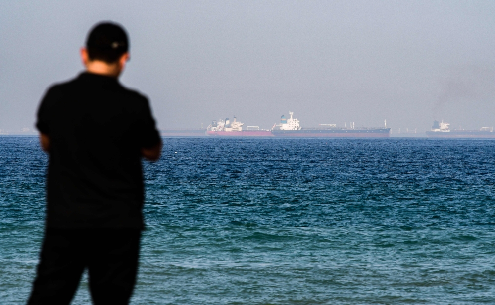 A man stands along a beach as tanker ships are seen in the waters of the Gulf of Oman off the coast of the eastern UAE emirate of Fujairah on June 15, 2019. / AFP / GIUSEPPE CACACE