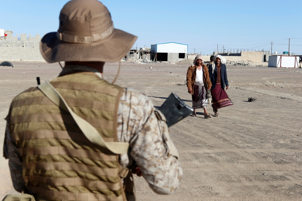 Yemenis walk past a Saudi soldier standing guard in Marib, January 26, 2018. Reuters/Faisal Al Nasser