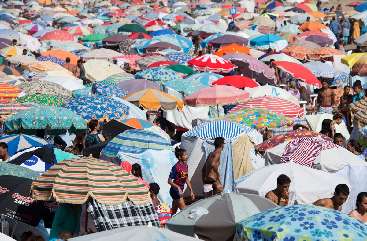 Moroccans walk between parasols at the beach in the Moroccan capital Rabat on August 21, 2016. AFP/ Fadel Senna