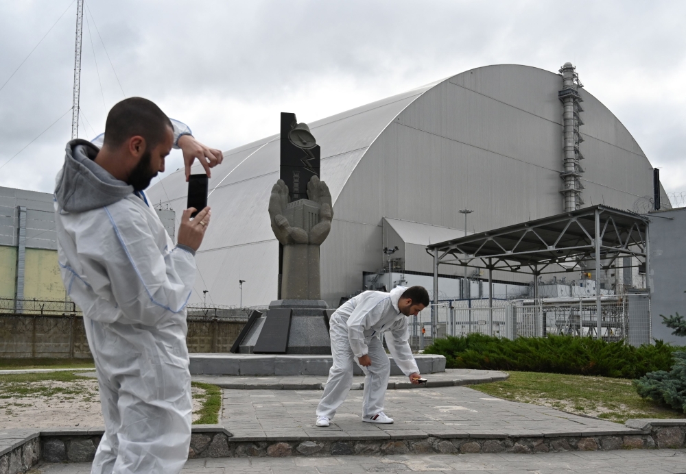 Tourists take pictures at New Safe Confinement (NSC), new metal dome encasing the destroyed reactor, at Chernobyl plant, Ukraine, on August 15, 2019. AFP / Genya Savilov 
