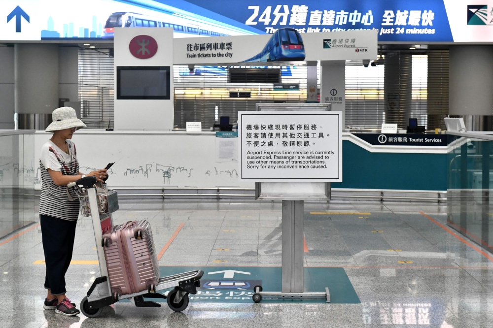 A woman stands next to a sign informing passengers the rail link between the airport and downtown is closed in Hong Kong on October 5, 2019, a day after the city's leader outlawed face coverings at protests invoking colonial-era emergency powers not used 