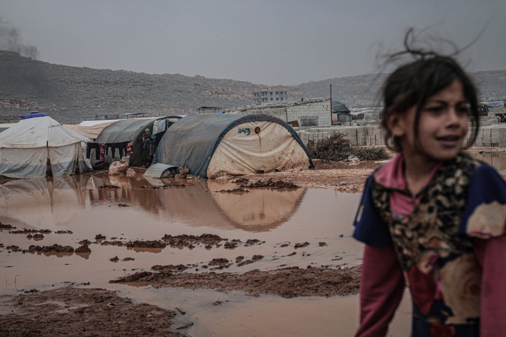 Syrians are seen on the mud-covered road between tents at a refugee camp, where Syrian refugees live, after heavy rain at winter season in northeastern Idlib, Syria on December 13, 2019. Muhammed Said - Anadolu 