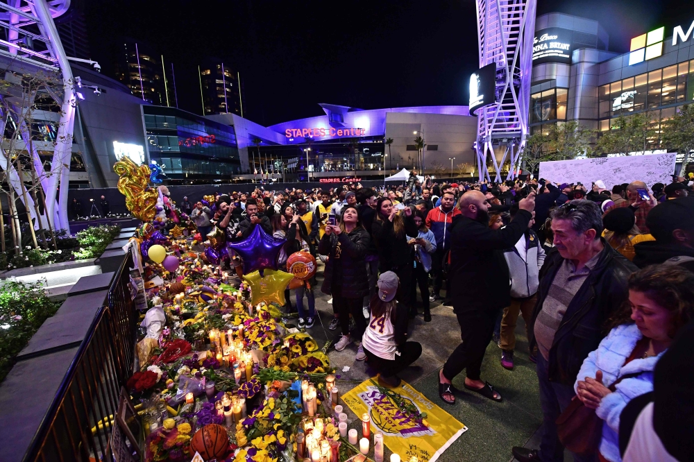 People gather in front of a makeshift memorial for former NBA and Los Angeles Lakers player Kobe Bryant and his daughter Gianna Bryant, who were killed with seven others in a helicopter crash on January 26, at LA Live plaza in front of Staples Center in L