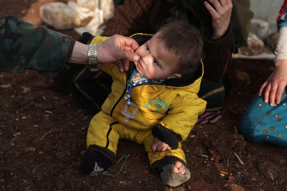 An internally displaced man pinches the cheek of a child wearing socks with a hole at a makeshift camp in Azaz, Syria February 19, 2020. Reuters/Khalil Ashawi
 