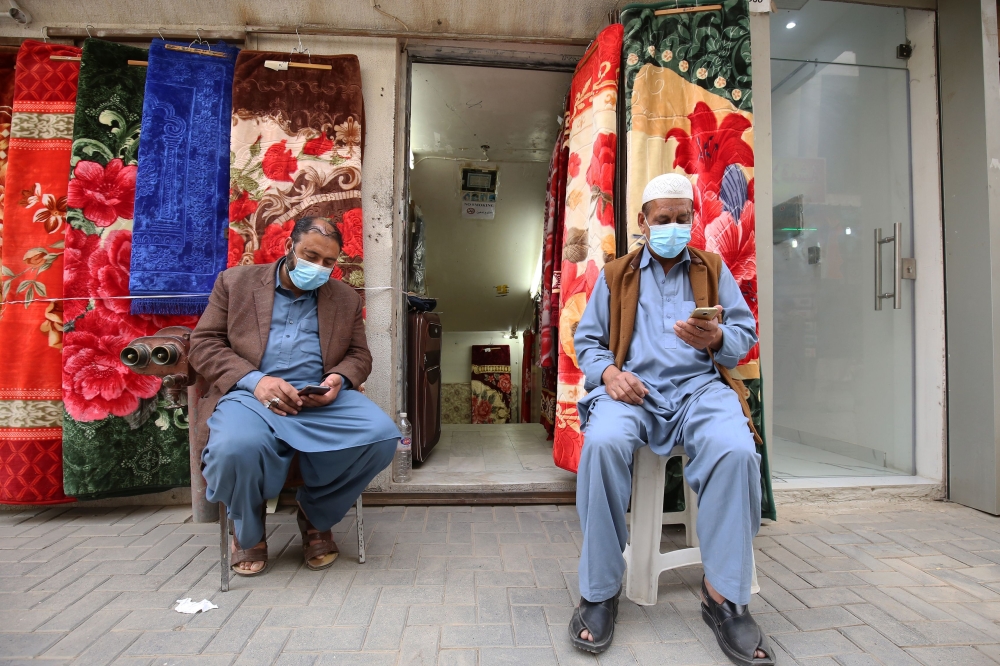 FILE PHOTO: Vendors, wearing protective masks, sit outside their shop in Kuwait City on February 26, 2020.  AFP / Yasser Al-Zayyat 