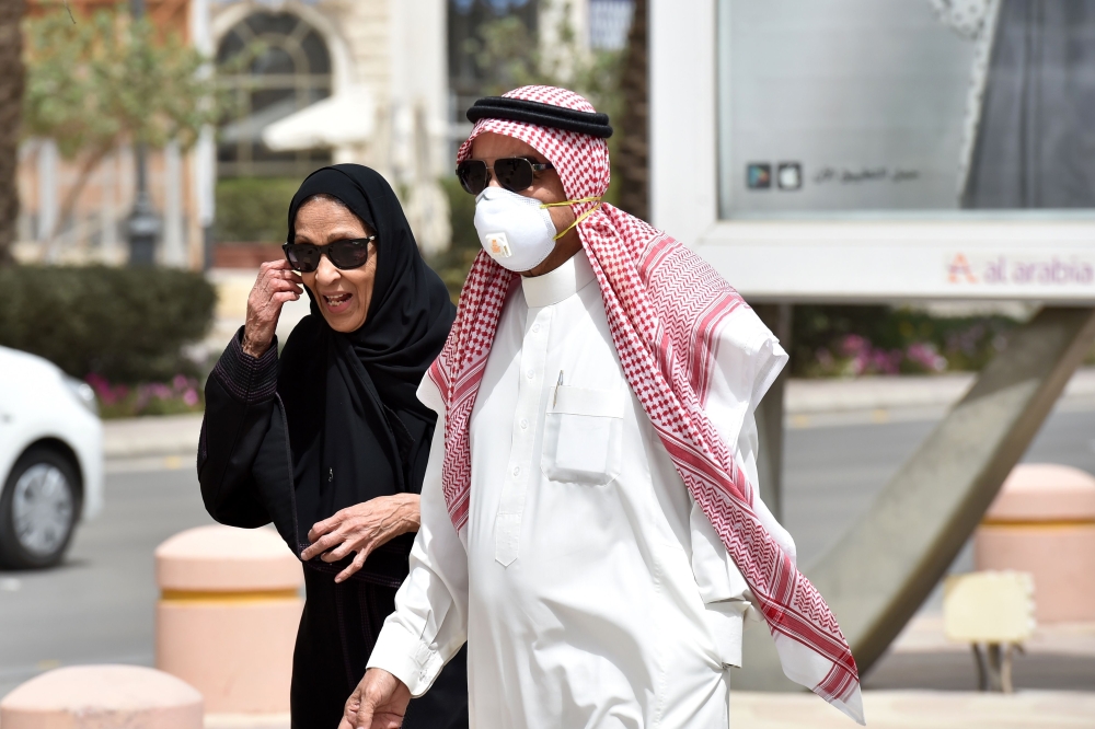 A Saudi man, wearing a protective mask as a precaution against COVID-19 coronavirus disease, walks with his wife along Tahlia street in the centre of the capital Riyadh on March 15, 2020. / AFP / FAYEZ NURELDINE