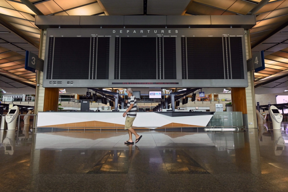 A man wearing a face mask walks past blank screen at the departure hall at Singapore Changi Airport's terminal 2, which is set to suspend operations for 18 months from May 1, 2020, as the COVID-19 coronavirus pandemic impacts the aviation sector, in Singa