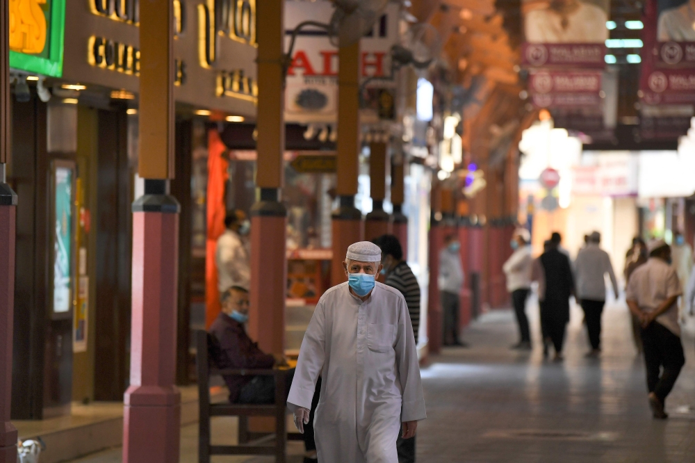 Men wearing face masks, due to the COVID-19 coronavirus pandemic, walk past jewellers' shops at the Dubai Gold Souk in the Gulf emirate on May 13, 2020, as markets re-open amidst an easing of pandemic restrictions. / AFP / Karim Sahib 