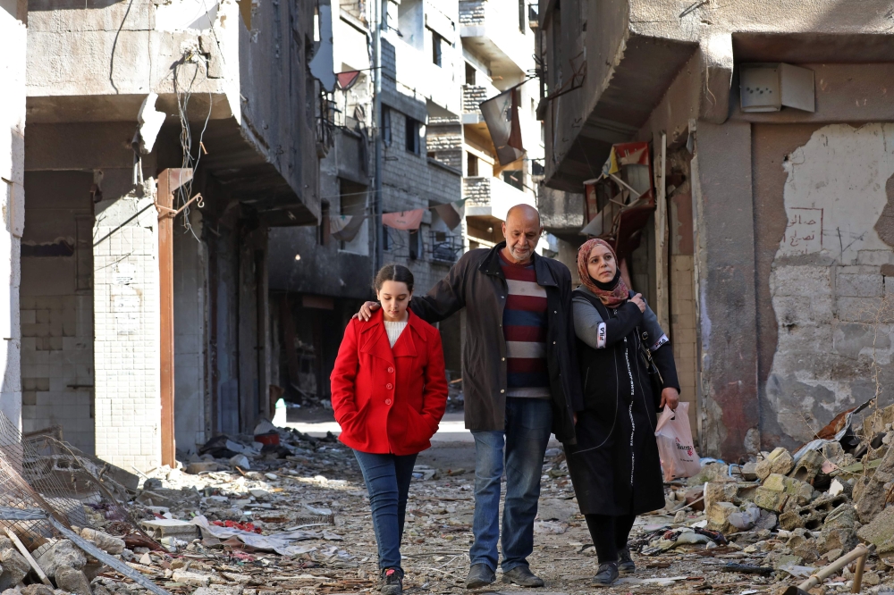 Issa al-Loubani, a 48-year-old Palestinian refugee, walks with his wife and daughter in a street in the Palestinian Yarmuk camp, on the southern outskirts of the Syrian capital Damascus, on November 25, 2020. AFP / LOUAI BESHARA