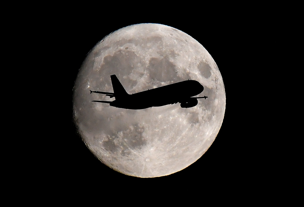 FILE PHOTO: A passenger plane passes in front of the moon as it makes its final landing approach to Heathrow Airport in London, Britain September 12, 2019. REUTERS/Toby Melville/File Photo