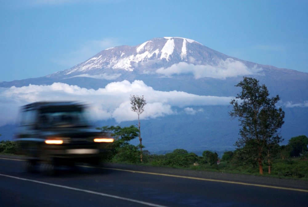 A vehicle drives past Mount Kilimanjaro in Tanzania's Hie district December 10, 2009. At the foot of Africa's snow-capped Mount Kilimanjaro, images of the mountain adorn the sides of rusting zinc shacks and beer bottle labels, but the fate of the real ver