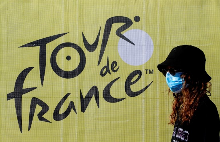 FILE PHOTO: August 26, 2020 A person wearing a protective face mask walks past a sign ahead of the Tour de France REUTERS/Eric Gaillard