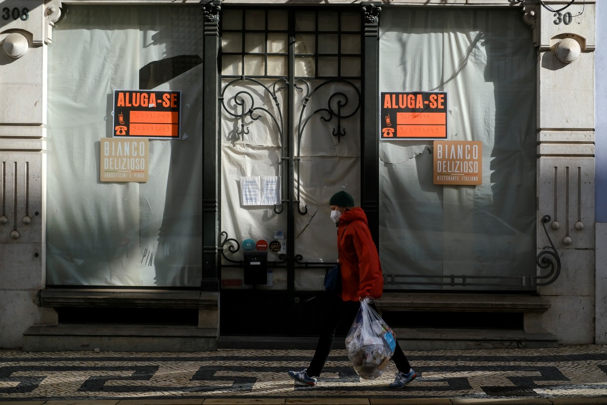 A woman wearing a protective mask due to coronavirus disease (COVID-19) pandemic walks past a closed store in central Lisbon, Portugal, November 25, 2021. REUTERS/Pedro Nunes
