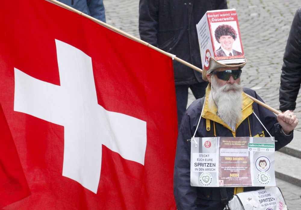 FILE PHOTO: A protestor carries a Swiss national flag during an unauthorised demonstration against COVID-19 restrictions in Zurich, Switzerland, October 30, 2021. REUTERS/Arnd WIegmann