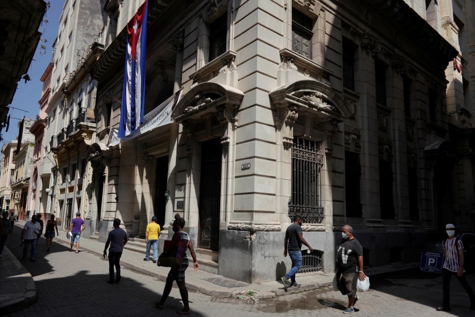 People walk under a Cuban flag at a commercial area amid concerns about the spread of the coronavirus disease (COVID-19), in Havana, Cuba, August 3, 2021. Picture taken August 3, 2021. REUTERS/Alexandre Meneghini

