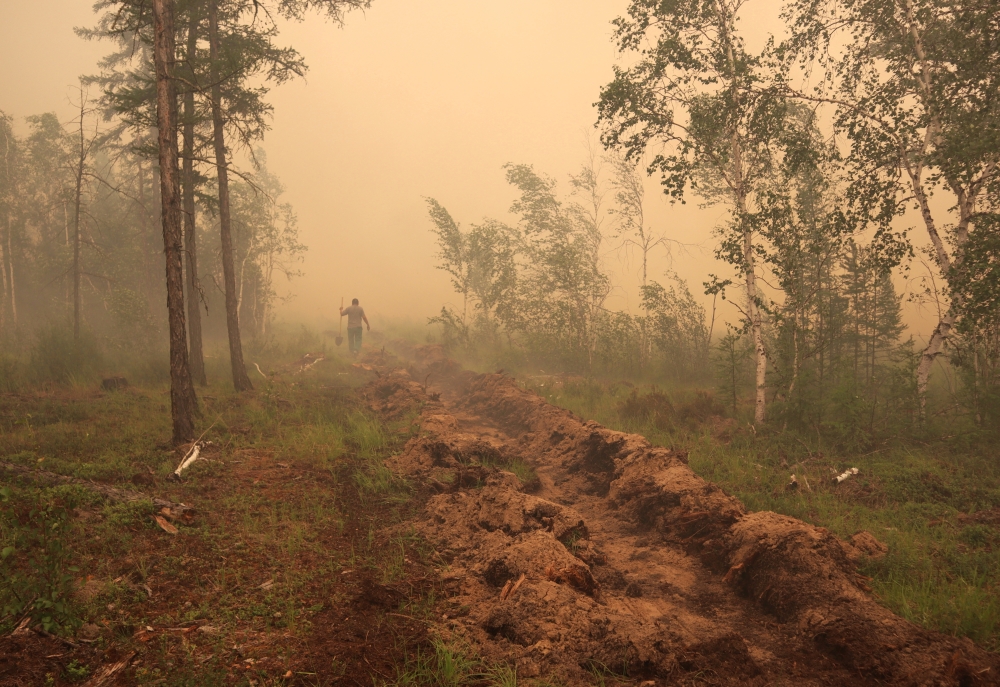 A man digs a control line during the work on extinguishing a forest fire near the village of Magaras in the region of Yakutia, Russia July 17, 2021. REUTERS/Roman Kutukov/File Photo