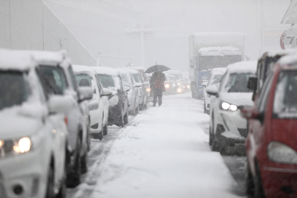 A person holding an umbrella walks among vehicles stuck in traffic in the Attiki Odos motorway, during heavy snowfall in Athens, Greece, January 24, 2022. REUTERS/Stelios Misinas