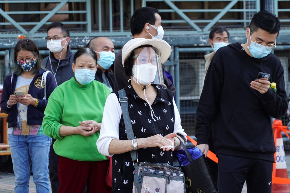 A woman wearing a face mask and a face shield lines up among people at a makeshift testing site for the coronavirus disease (COVID-19) following the outbreak, in Hong Kong, China February 11, 2022. REUTERS/Joyce Zhou
