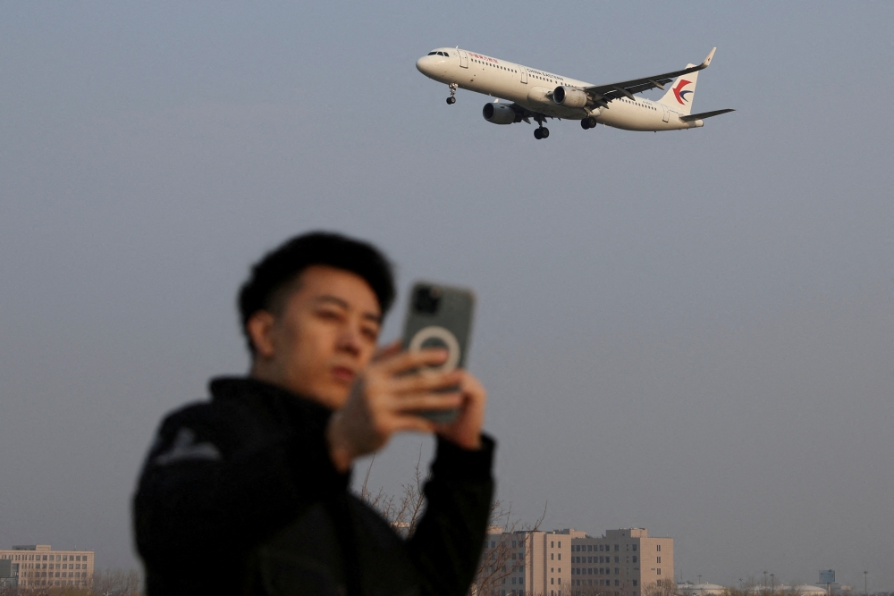 FILE PHOTO: A man takes a selfie as a plane of China Eastern Airlines lands at the Beijing Capital International Airport in Beijing, China March 23, 2022. REUTERS