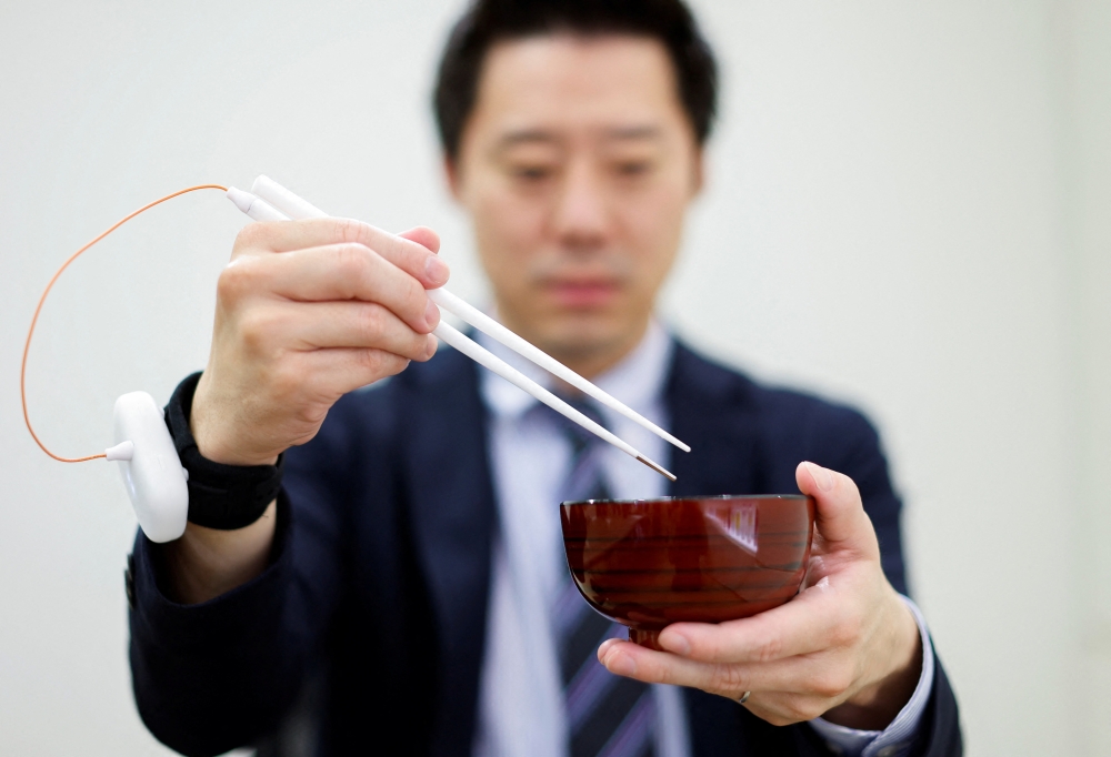 An employee of Kirin Holdings demonstrates chopsticks that can enhance food taste using an electrical stimulation waveform that was jointly developed by the company and Meiji University's School of Science and Technology Professor Homei Miyashita, in Tokyo, Japan April 15, 2022. REUTERS/Issei Kato