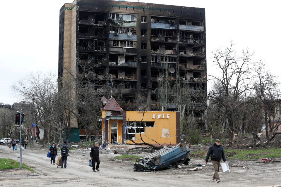 People walk past a residential building heavily damaged during Ukraine-Russia conflict in the southern port city of Mariupol, Ukraine April 21, 2022. REUTERS/Alexander Ermochenko

