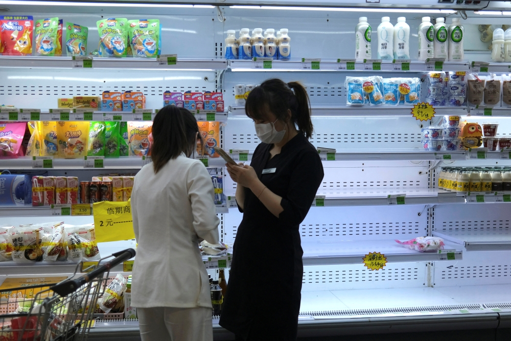 Customers shop in front of a half-empty freezer for diary products, following the coronavirus disease (COVID-19) outbreak, at a supermarket in Beijing, China April 25, 2022. REUTERS/Tingshu Wang