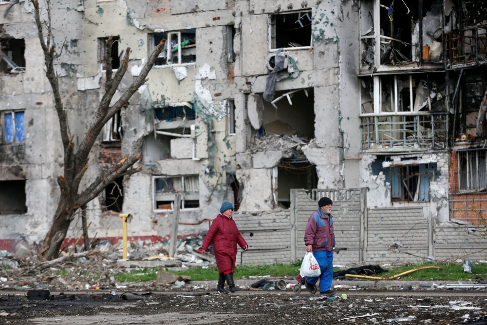 People walk near a residential building destroyed during Ukraine-Russia conflict in the southern port city of Mariupol, Ukraine April 22, 2022. REUTERS/Alexander Ermochenko/File Photo