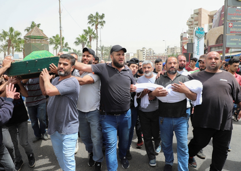 People carry the coffin of a woman as a father holds the body of his child who both died after a small dinghy carrying around 60 people sunk off the coast near the port city of Tripoli on Saturday night, during a funeral in Tripoli, Lebanon April 25, 2022. REUTERS/Mohamed Azakir