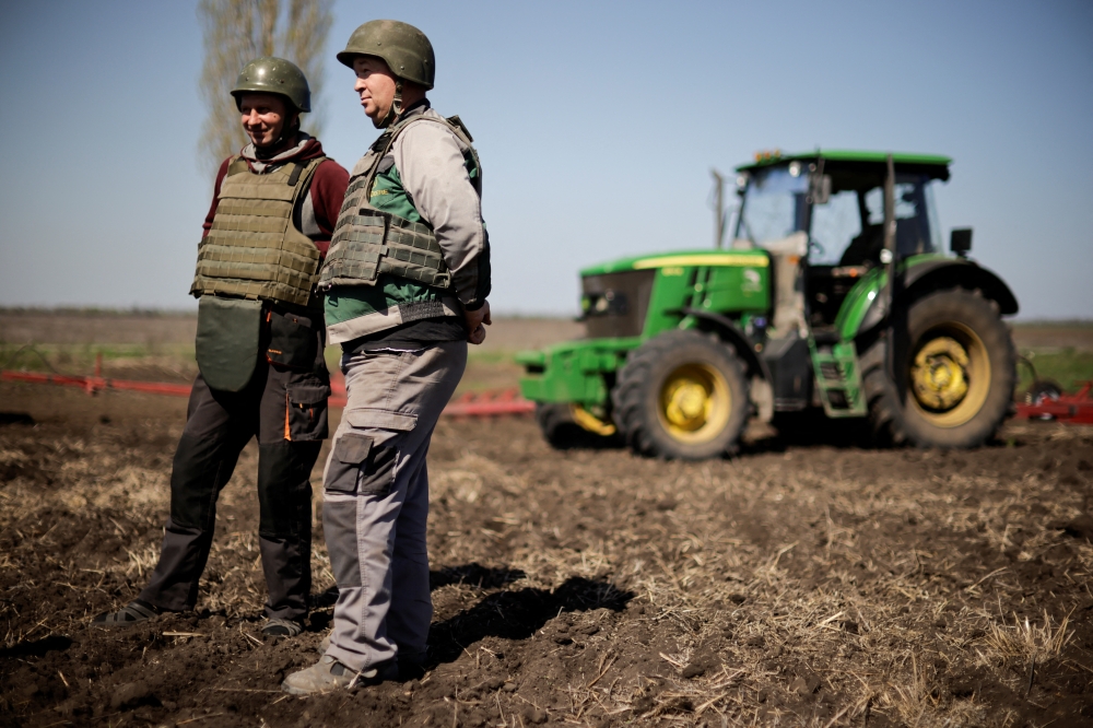 Yuri and Oleksiy, Ukrainian farmers wearing body armours and helmets, work at the topsoil in a field, amid Russia's invasion of Ukraine, in Zaporizhzhia region, Ukraine April 26, 2022. REUTERS/Ueslei Marcelino