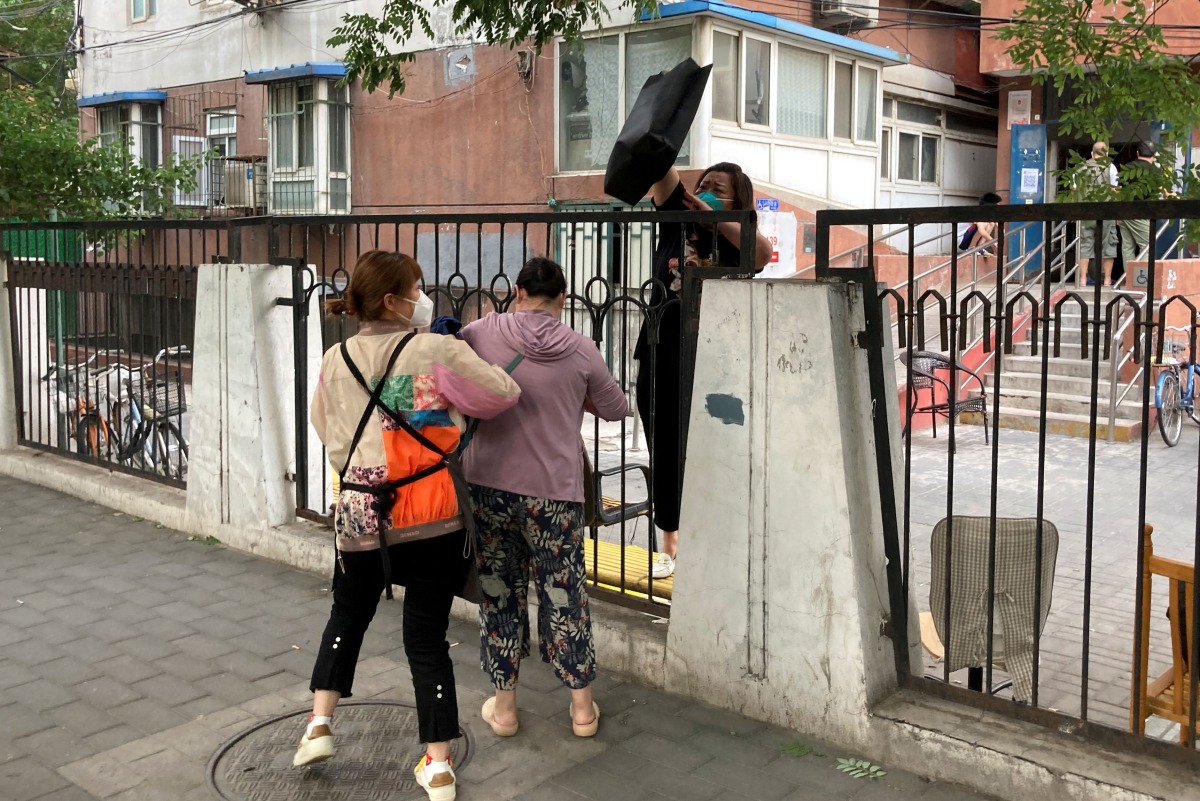 A resident fetches a bag over the fence at a residential compound that is under lockdown, following the coronavirus disease (COVID-19) outbreak, in Chaoyang district of Beijing, China June 12, 2022. REUTERS/Martin Pollard
