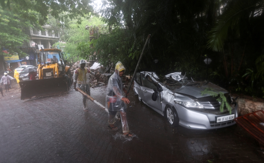 People walk past a damaged car after a wall of a residential society collapsed on it amidst heavy rainfall in Mumbai, India, July 5, 2022. REUTERS/Francis Mascarenhas/File Photo