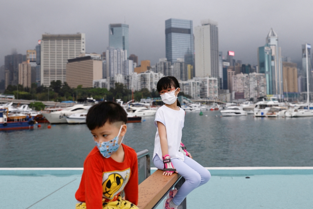 Children wearing face masks rest next to Victoria Harbour, amid the coronavirus disease (COVID-19) pandemic, in Hong Kong, China, March 25, 2022. REUTERS/Tyrone Siu/File Photo