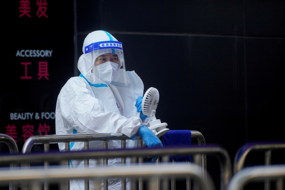 A medical worker in a protective suit uses a fan at a nucleic acid testing station, following the coronavirus disease (COVID-19) outbreak, amid a heatwave warning in Shanghai, China, on August 23, 2022. REUTERS/Aly Song