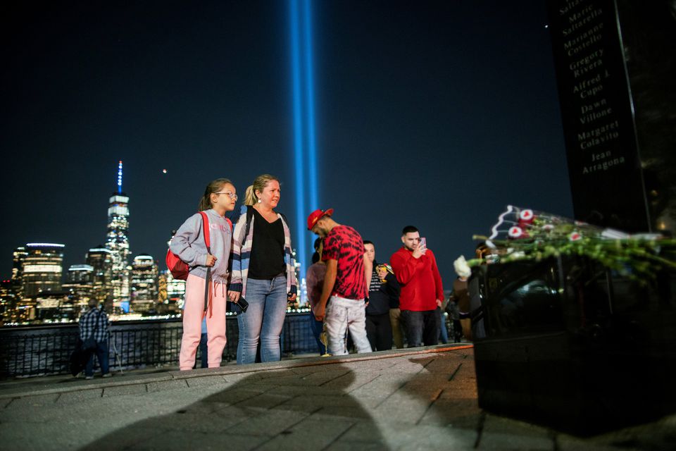 People pay respect for the victims at a memorial while the Tribute in Light art installation and the One World Trade Center are seen in the background on the 20th anniversary of the September 11, 2001 attacks in New York City, as it is seen from Exchange Place, New Jersey, US, on September 11, 2021. REUTERS/Eduardo Munoz