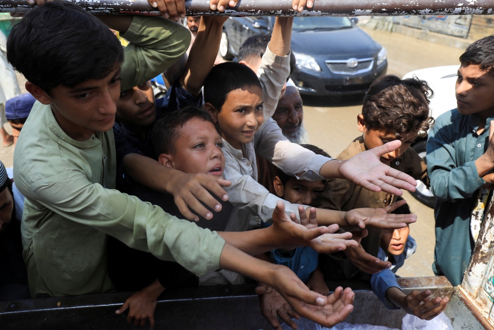 Boys, victims of the flood, reach out for food from a relief worker, following rains and floods during the monsoon season in Nowshera, Pakistan, August 30, 2022. (REUTERS/Fayaz Aziz)