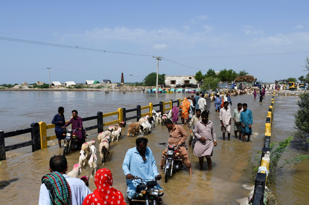 People cross a bridge amid flood waters, following rains and floods during the monsoon season in Puran Dhoro, Badin, Pakistan August 30, 2022. Reuters/Yasir Rajput