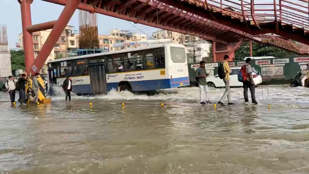 People walk next to a bus driving along a waterlogged road in Bengaluru, Karnataka state, India in this screen grab taken from a social media video September 5, 2022. Mallika Nallusamy/via REUTERS