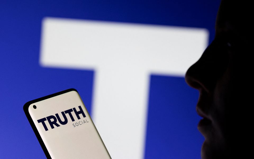 The Truth social network logo is seen displayed behind a woman holding a smartphone in this picture illustration taken on February 21, 2022. REUTERS/Dado Ruvic/Illustration