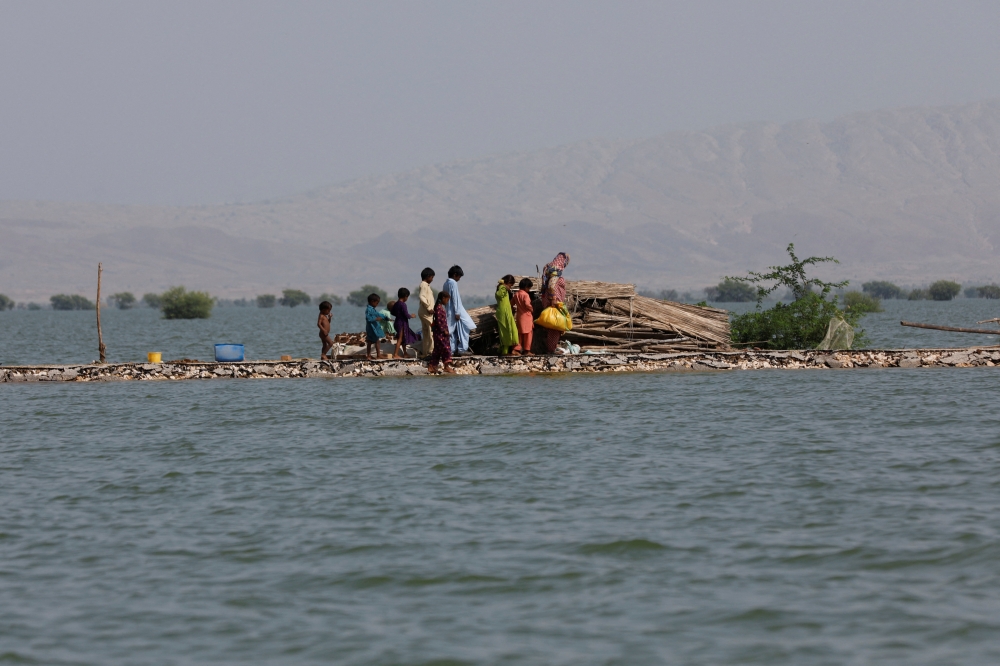 A woman and children walk as they taking refuge along a damaged road amid flood, following rains and floods during the monsoon season in Bajara village, at the banks of Manchar lake, in Sehwan, Pakistan, September 6, 2022. (REUTERS/Akhtar Soomro)