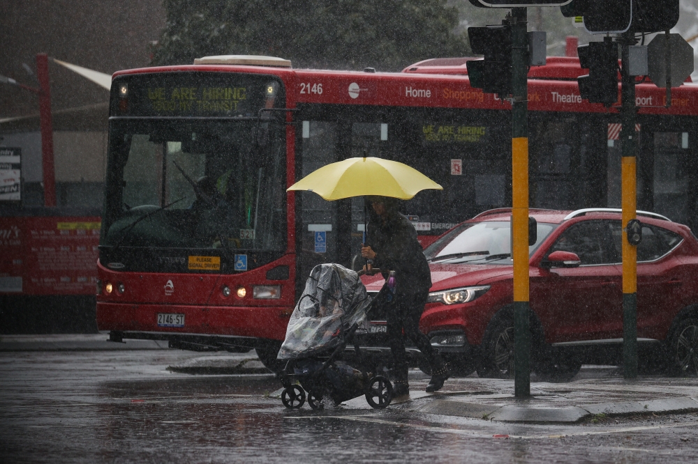 A pedestrian pushing a baby pram crosses a flooding intersection as heavy rains affect Sydney, Australia, October 6, 2022. REUTERS/Loren Elliott