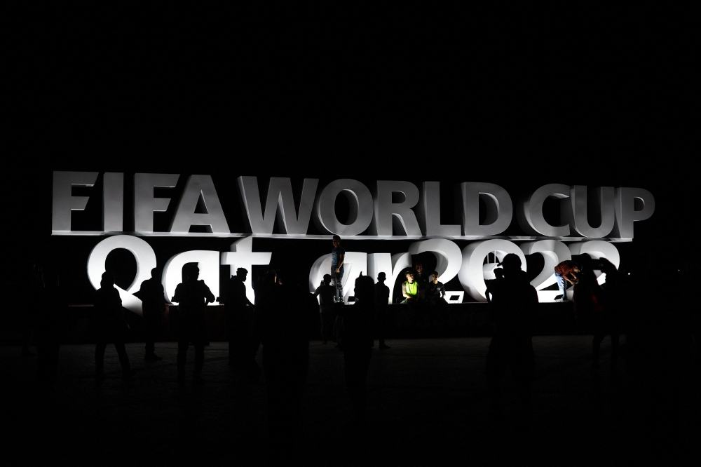 People relax in front of a FIFA World Cup sign on the Doha Corniche on November 13, 2022. (REUTERS/Hannah Mckay)