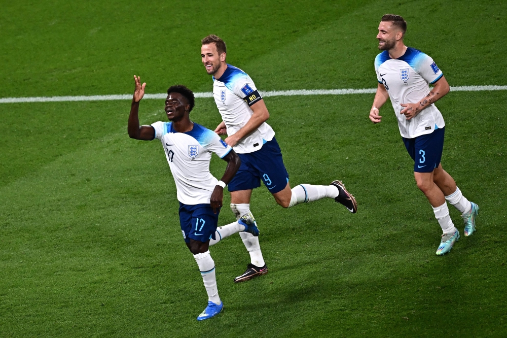 England's forward Bukayo Saka (left) celebrates teammates Harry Kane (centre) and England's defender #03 Luke Shaw after he scored England's fourth goal during the Qatar 2022 World Cup Group B football match between England and Iran at the Khalifa International Stadium in Doha on November 21, 2022. (Photo by Anne-Christine POUJOULAT / AFP)