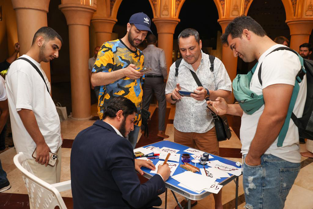 Tourists stand near an artist who is doing an Arabic calligraphy.